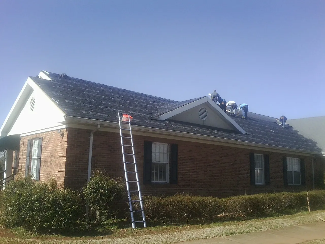 Crew tearing shingles off a brick ranch roof with a ladder set — Metal Roof Repair work by our crew in Warren